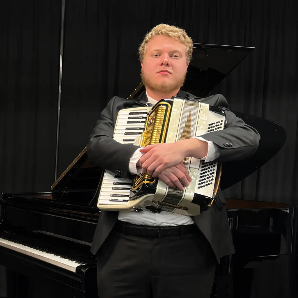 Young male musician holding accordion beside grand piano