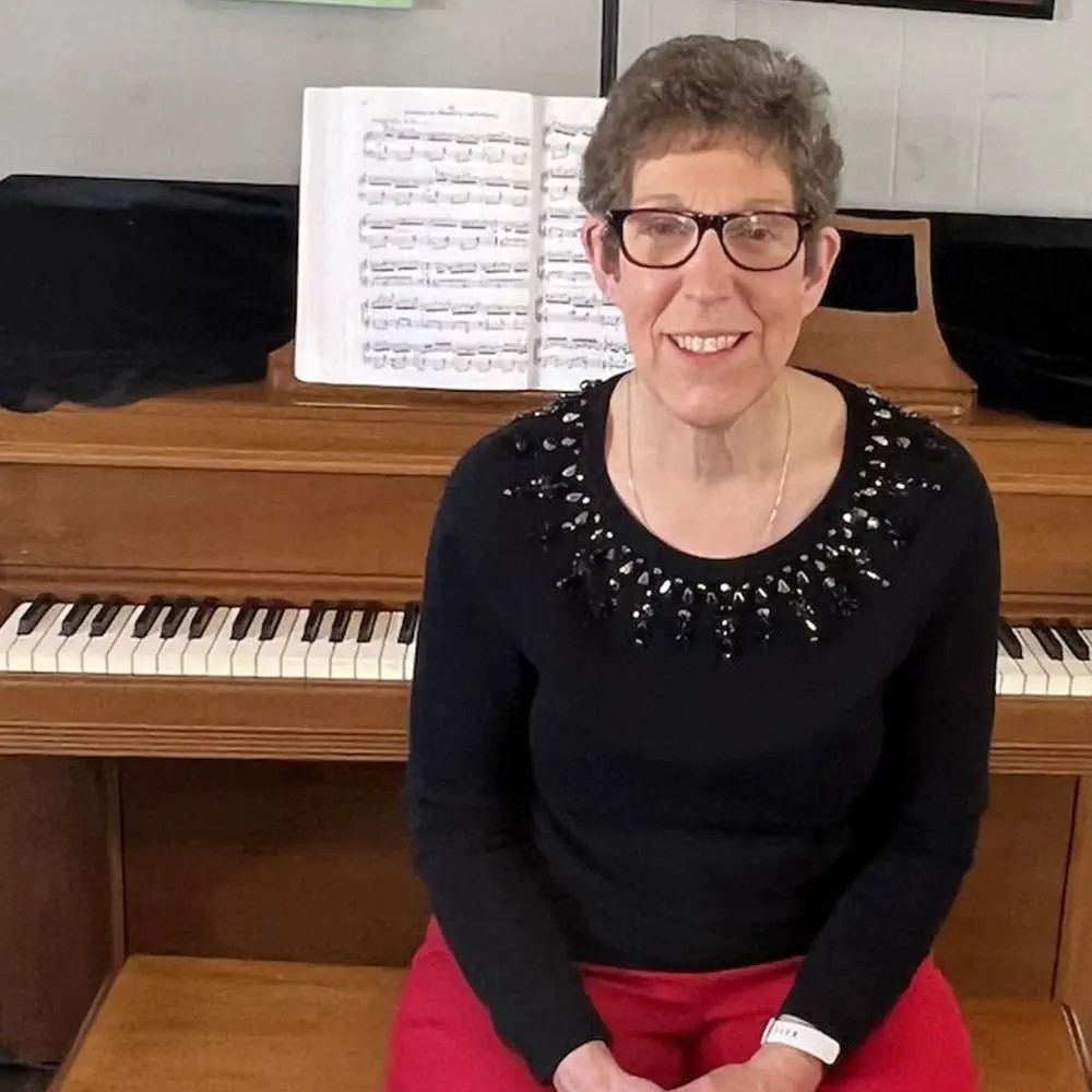 Smiling woman sitting in front of upright piano with sheet music