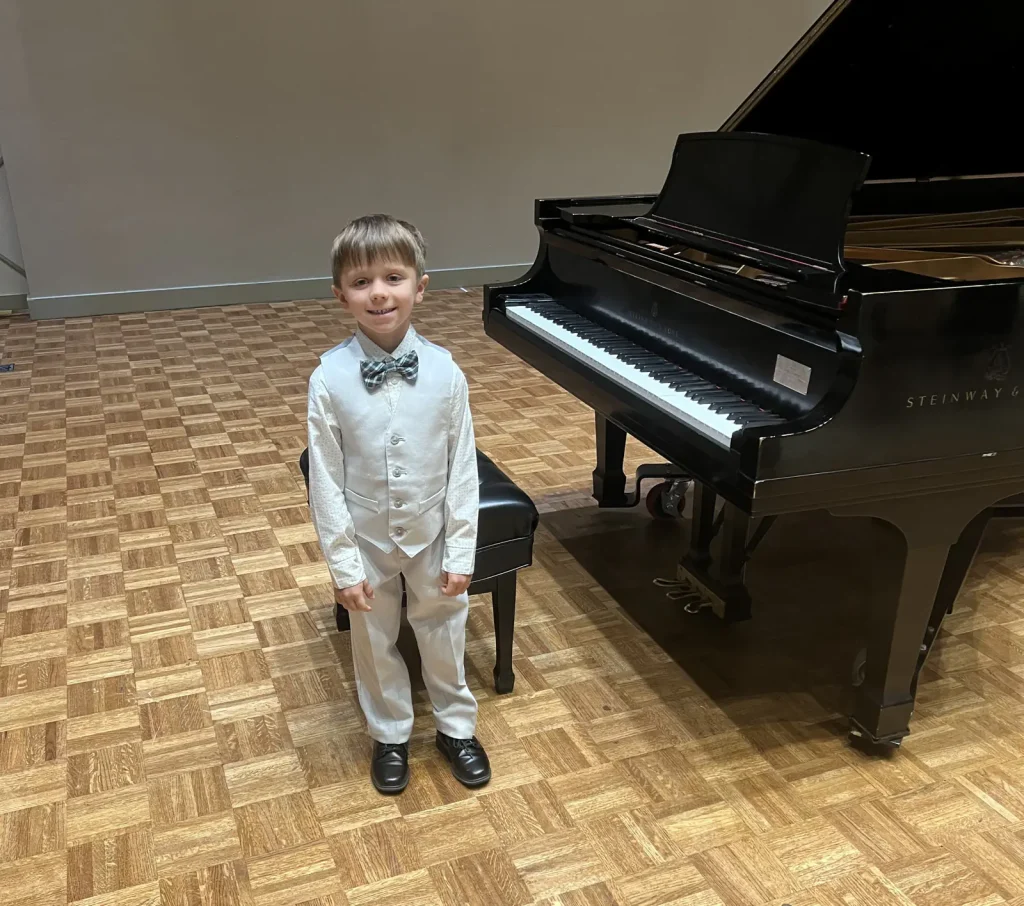 Young boy in white suit beside Steinway grand piano