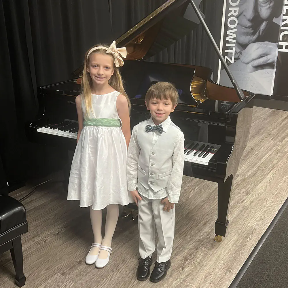 Two young children dressed formally beside a grand piano
