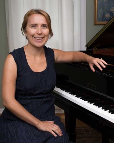 Smiling woman in navy dress seated beside grand piano