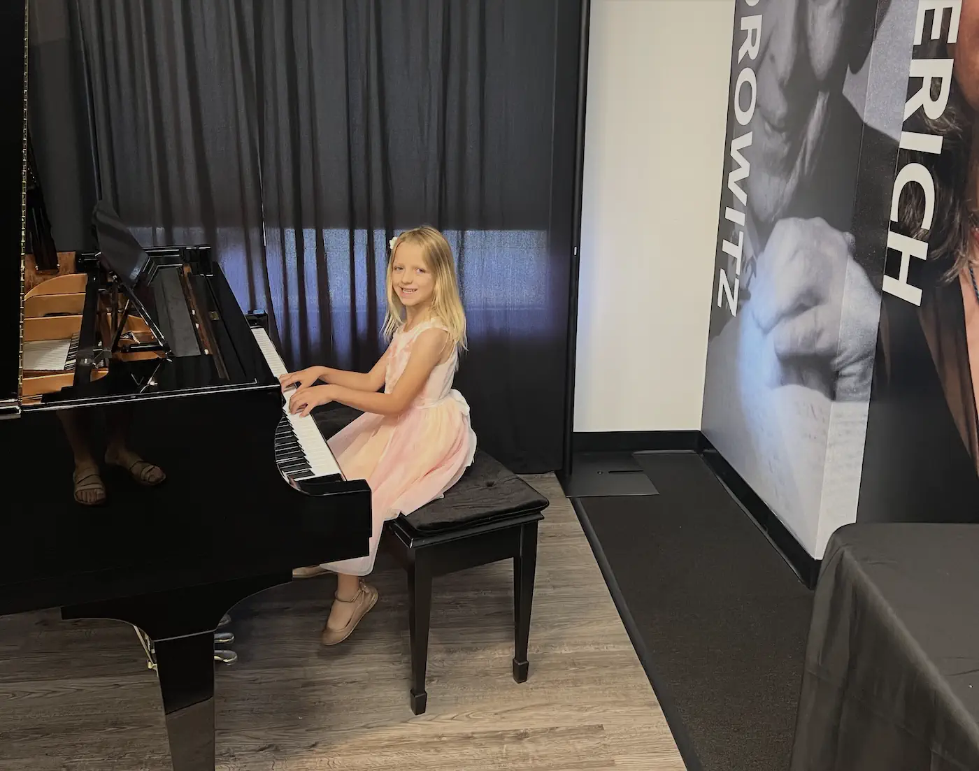 Young girl in pink dress playing grand piano at recital