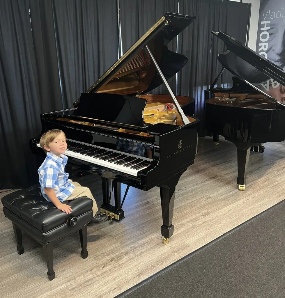 Young boy smiling at Steinway grand piano showroom