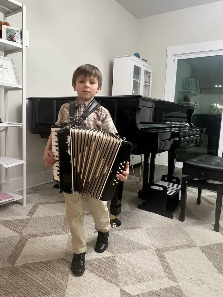 Young boy playing black accordion in music room