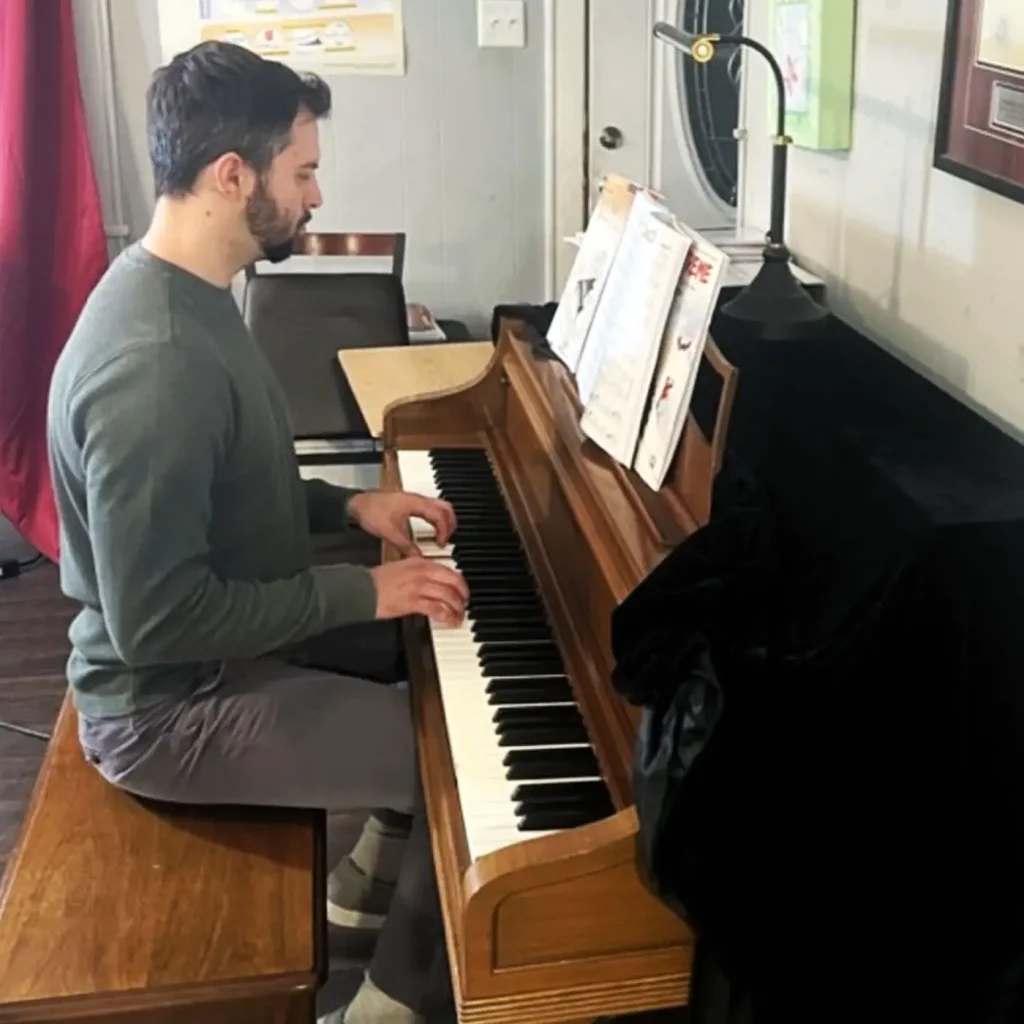 Bearded man playing upright piano with sheet music