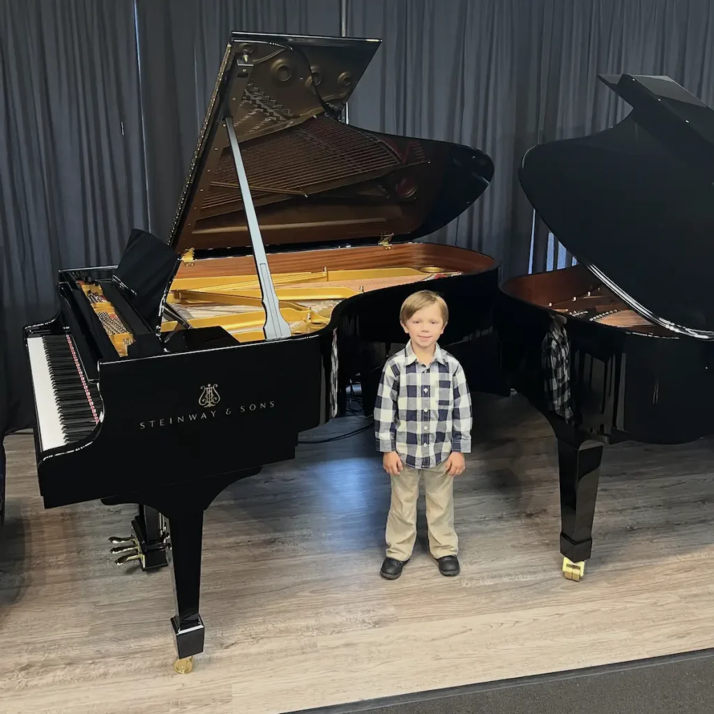 Young boy standing between two Steinway grand pianos