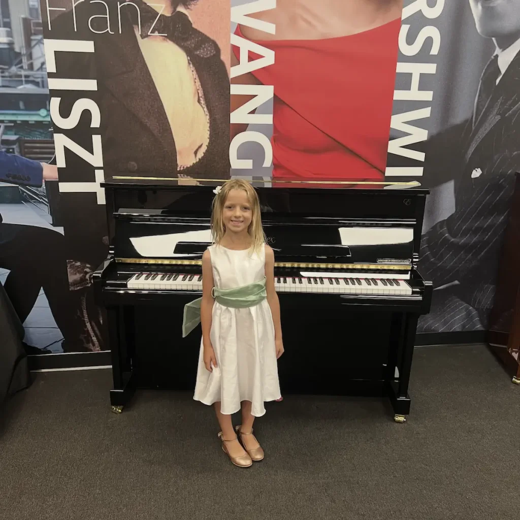 Young girl in white dress standing before upright piano