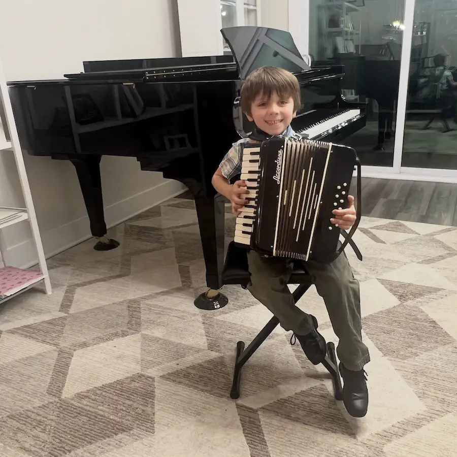 Young boy smiling while playing accordion near grand piano