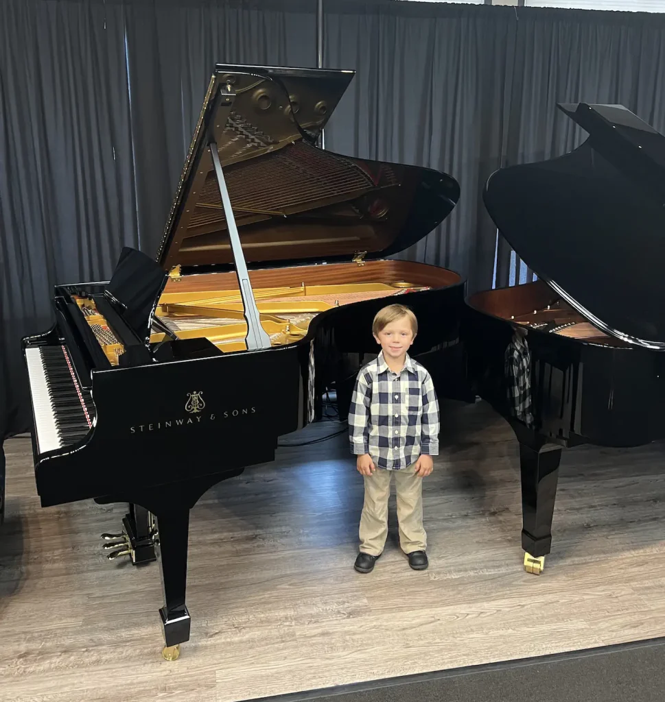 Young boy standing between two Steinway grand pianos
