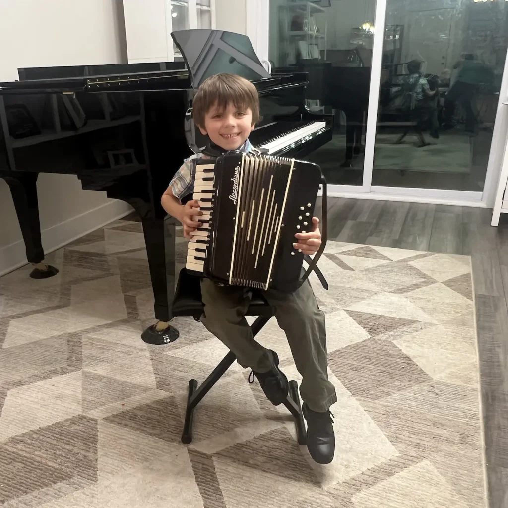 Young boy smiling while playing accordion near grand piano