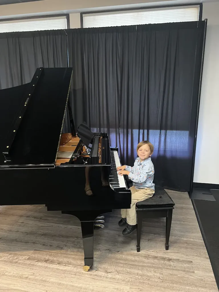 Young boy smiling while playing a black grand piano