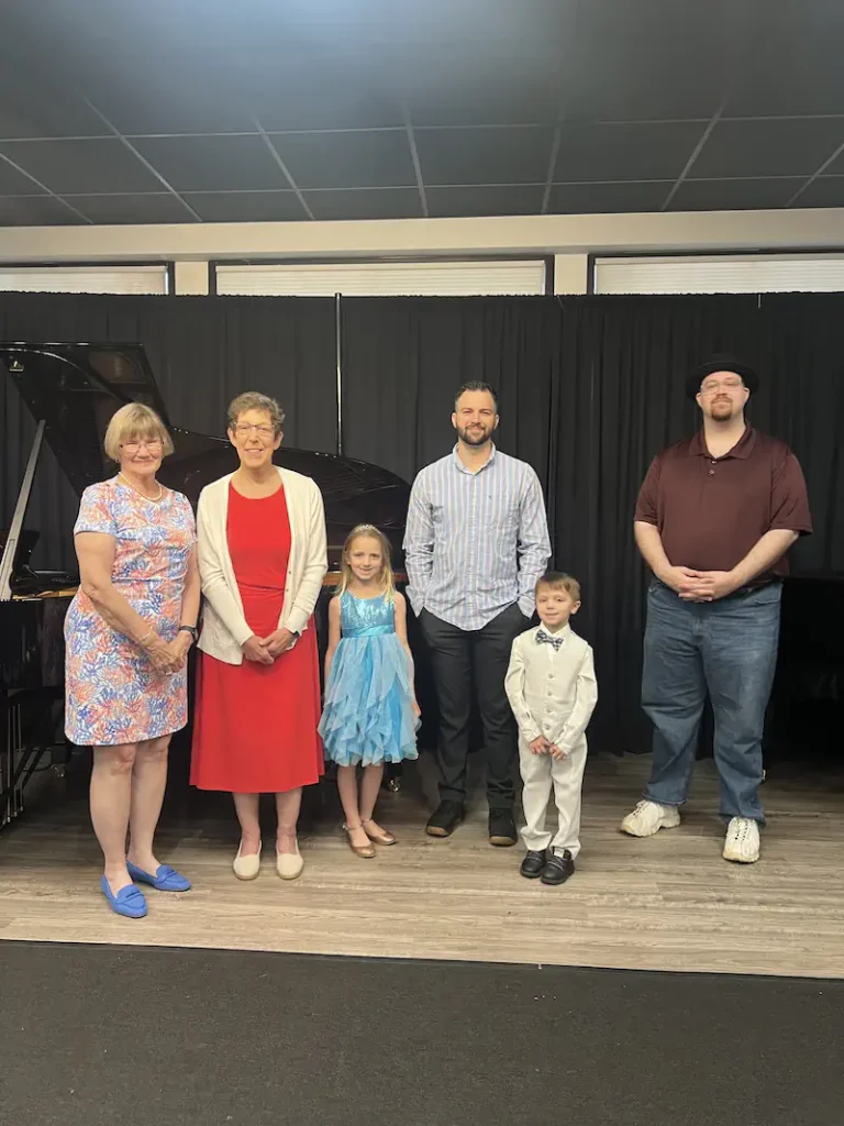 Group of six people posing after piano recital on stage