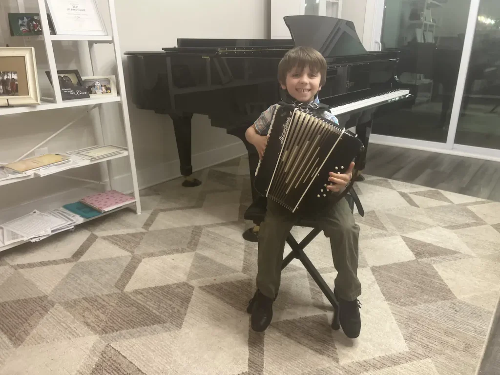 Young boy smiling while holding an accordion near grand piano