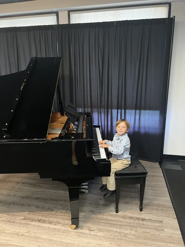 Young boy smiling while playing black grand piano