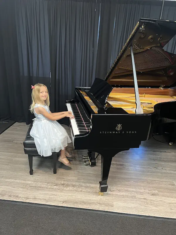 Young girl in white dress playing Steinway grand piano